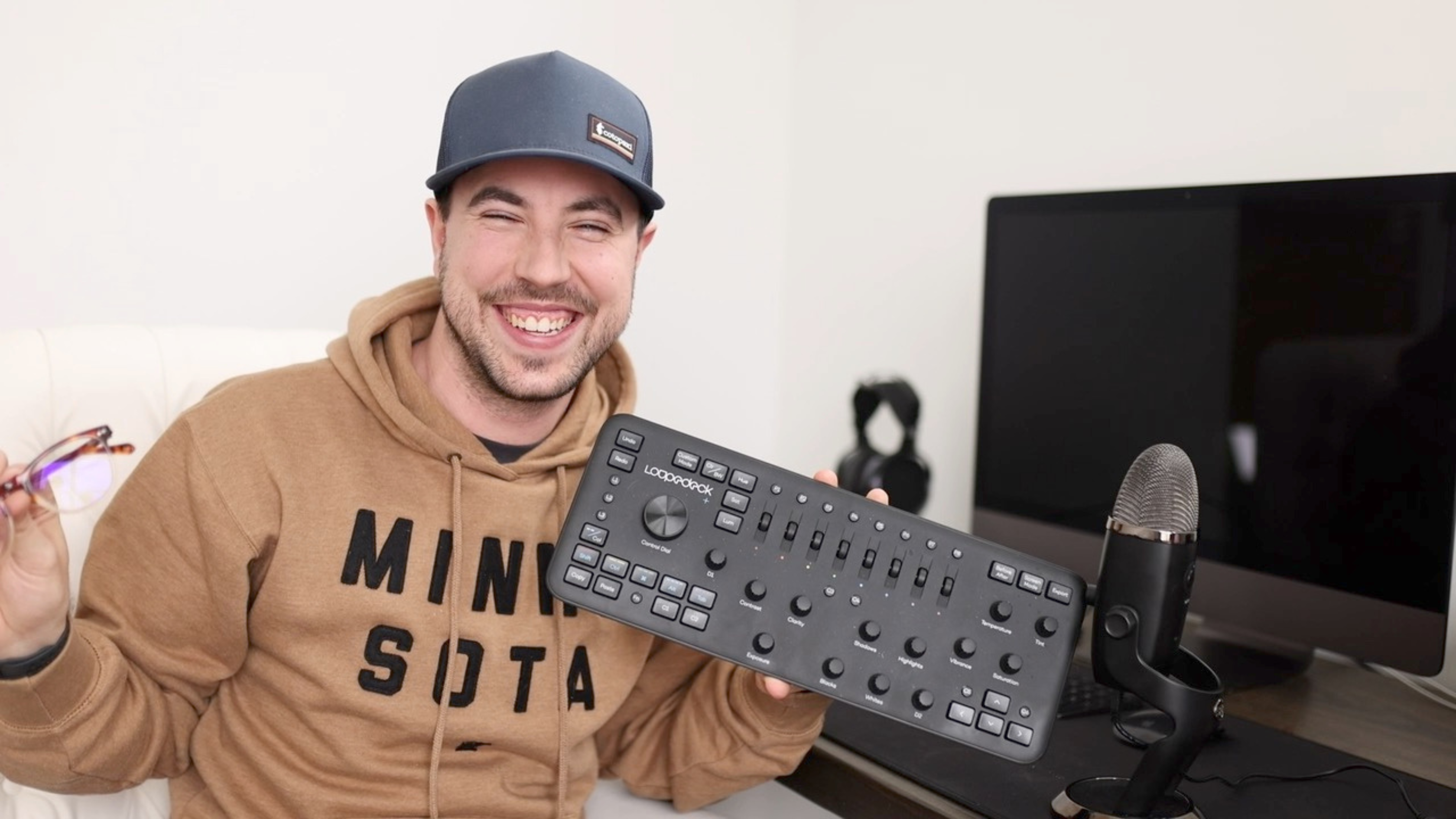 A photographer sitting in front of his desk holding up a Loupedeck, an editing tool for photography