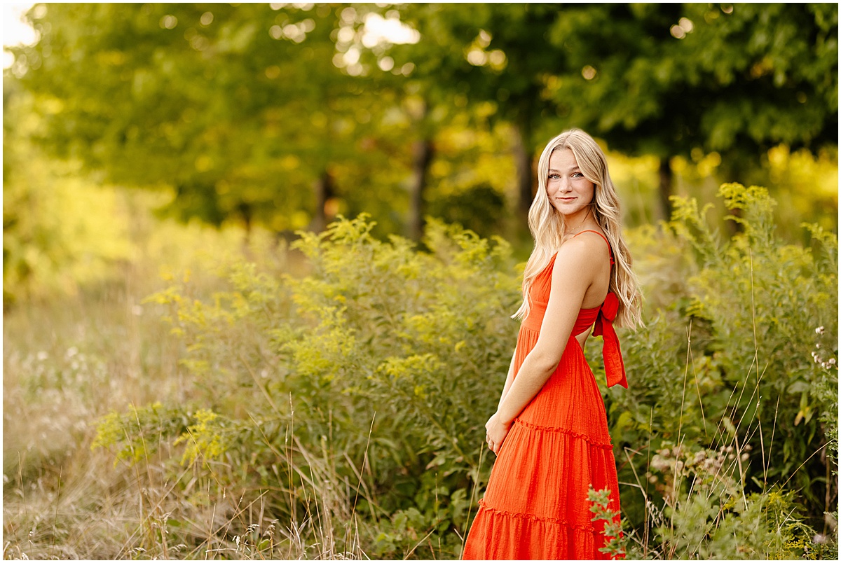 High school senior Abby at the Minnesota Landscape Arboretum in front of a beautiful field in a long orange dress