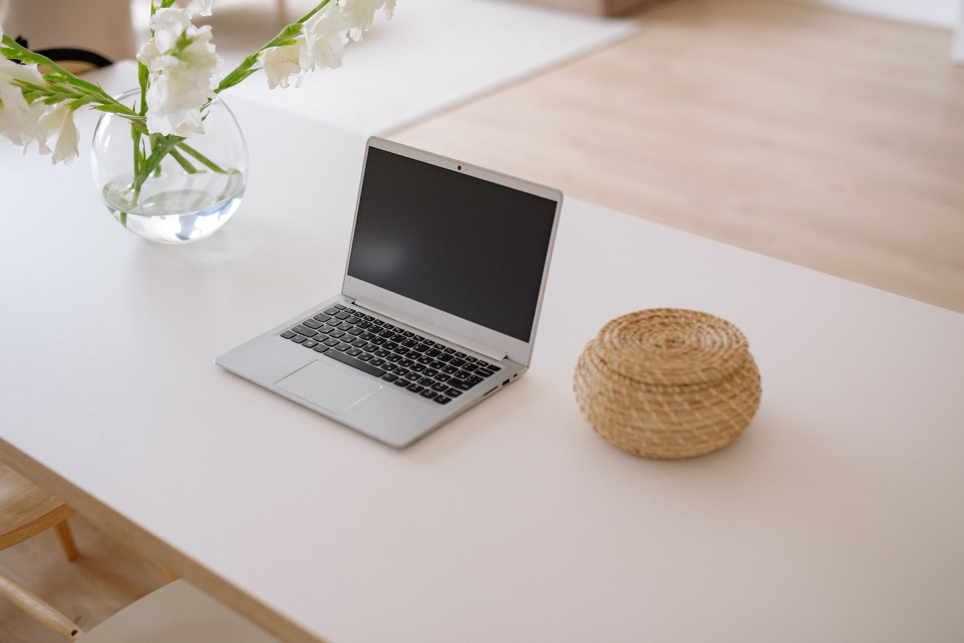 laptop with basket and white flowers in glass vase on a desk