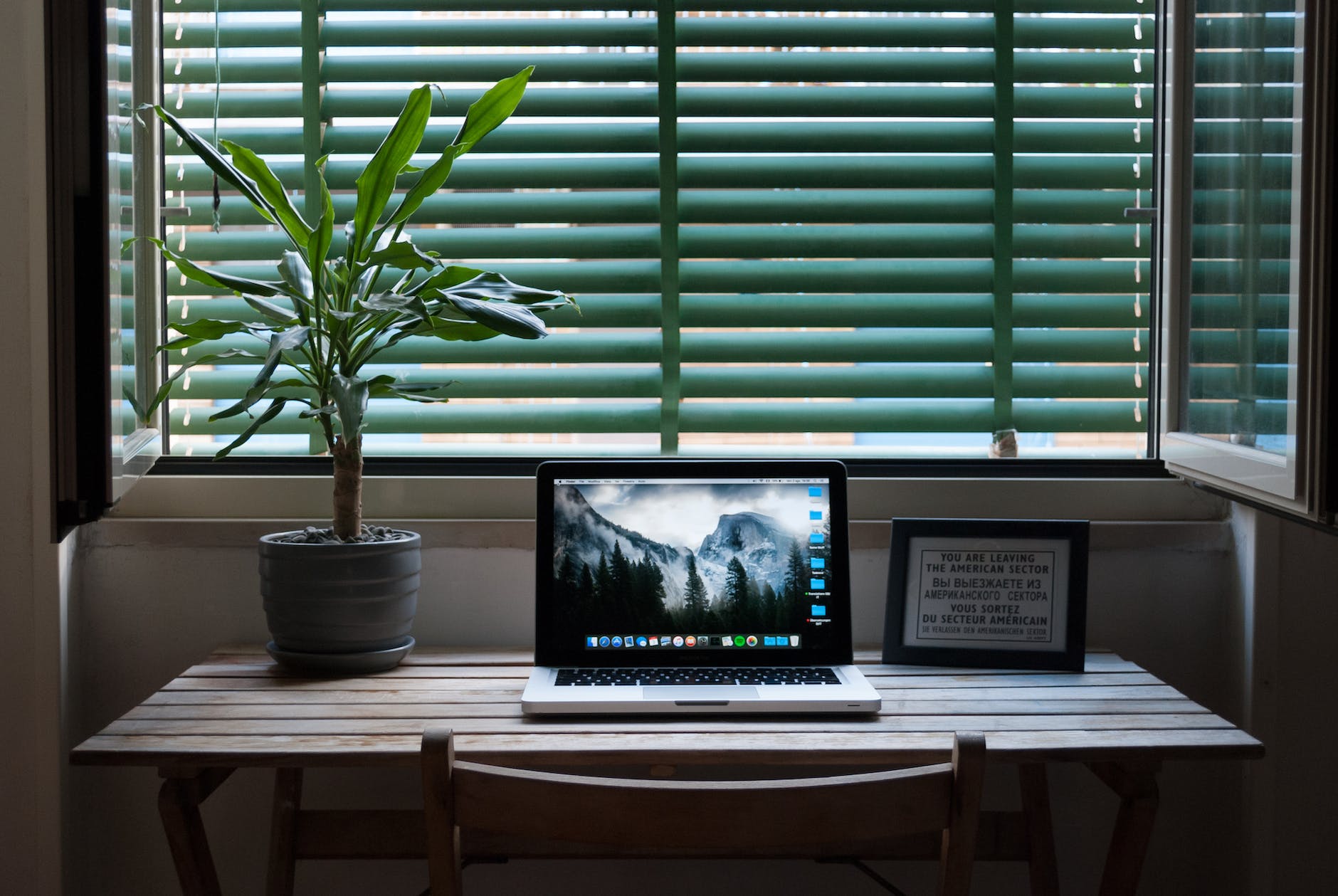 photo of macbook air on a table next to house plant and picture frame
